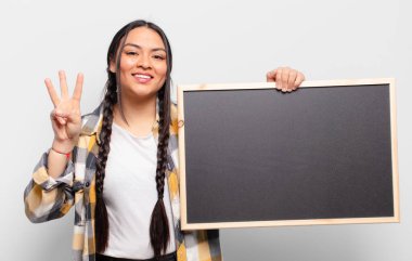 İspanyol kadın gülümsüyor ve arkadaş canlısı görünüyor. Üç ya da üç numarayı gösteriyor. Elleri önde, geri sayıyor.