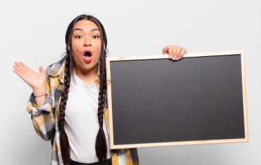 İspanyol kadın şaşırmış ve şoka uğramış görünüyor, çenesi düşmüş, eli açık bir objeyi tutuyor.