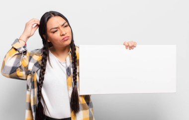 İspanyol kadın şaşkın ve şaşkın hissediyor, kafasını kaşıyor ve yan tarafa bakıyor.