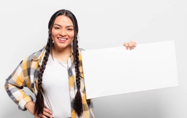 İspanyol kadın mutlu bir şekilde gülümsüyor, eli kalçasında ve kendinden emin, olumlu, gururlu ve arkadaş canlısı bir tavırla.