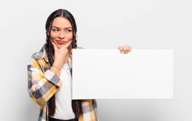 İspanyol kadın mutlu, kendinden emin bir ifadeyle gülümsüyor, çenesinde elleri, merak ediyor ve yan tarafa bakıyor.