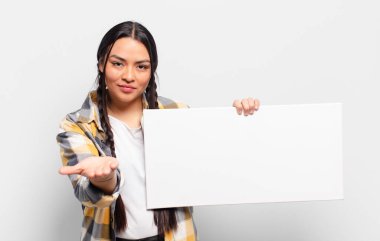 İspanyol kadın mutlu bir şekilde gülümsüyor arkadaş canlısı, kendinden emin, olumlu bakışlı, bir nesne ya da konsept sunuyor ve gösteriyor.