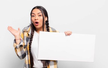 İspanyol kadın şaşırmış ve şoka uğramış görünüyor, çenesi düşmüş, eli açık bir objeyi tutuyor.