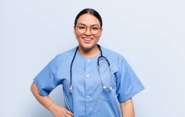 İspanyol kadın mutlu bir şekilde gülümsüyor, eli kalçasında ve kendinden emin, olumlu, gururlu ve arkadaş canlısı bir tavırla.