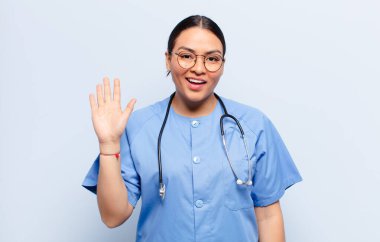 İspanyol kadın mutlu ve neşeli bir şekilde gülümsüyor, el sallıyor, seni selamlıyor ve selamlıyor, ya da hoşça kal diyor.