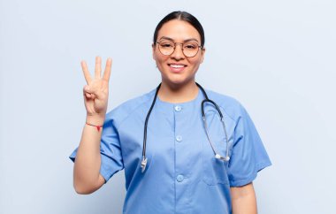 İspanyol kadın gülümsüyor ve arkadaş canlısı görünüyor. Üç ya da üç numarayı gösteriyor. Elleri önde, geri sayıyor.