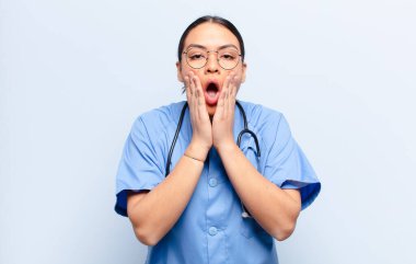 İspanyol kadın şok olmuş ve korkmuş hissediyor, ağzı açık ve elleri yanaklarında korkmuş görünüyor.