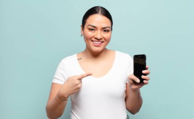 İspanyol kadın neşeli bir şekilde gülümsüyor, mutlu hissediyor ve kenarı ve yukarıyı işaret ediyor, fotokopi uzayındaki nesneleri gösteriyor