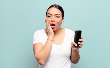 İspanyol kadın şok olmuş ve korkmuş hissediyor, ağzı açık ve elleri yanaklarında korkmuş görünüyor.