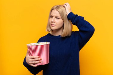 Sarışın kadın şaşkın ve şaşkın hissediyor, kafasını kaşıyor ve yan tarafa bakıyor.