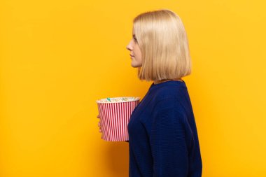 Profil görünümlü sarışın kadın ilerideki boşluğu kopyalamaya çalışıyor, düşünüyor, hayal ediyor ya da hayal kuruyor.