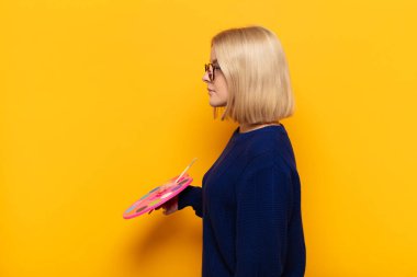 Profil görünümlü sarışın kadın ilerideki boşluğu kopyalamaya çalışıyor, düşünüyor, hayal ediyor ya da hayal kuruyor.