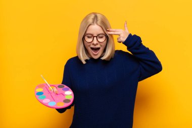 Sarışın kadın mutsuz ve stresli görünüyor, intihar jesti elle silah işareti yapıyor, kafasını işaret ediyor.