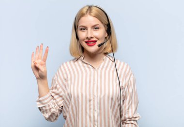 Sarışın kadın gülümsüyor ve arkadaş canlısı görünüyor, 4 ya da 4 numarayı gösteriyor, eli önde, geriye doğru sayıyor.