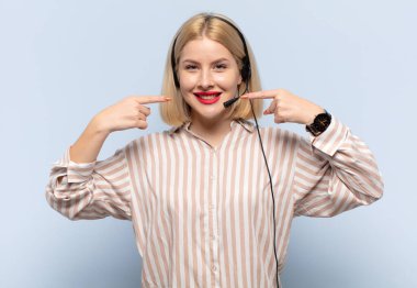 Sarışın kadın kendine güvenerek gülümsüyor. Geniş gülüşünü gösteriyor. Olumlu, rahat, tatmin olmuş bir tavır.