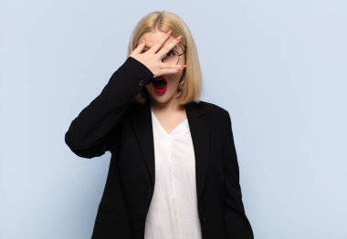 Sarışın kadın şok olmuş, korkmuş ya da korkmuş görünüyordu. Yüzü elle kaplıydı ve parmaklarının arasından bakıyordu.