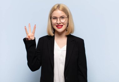 Sarışın kadın gülümsüyor ve arkadaş canlısı görünüyor, üç ya da üç numarayı gösteriyor, eli önde, geriye doğru sayıyor.