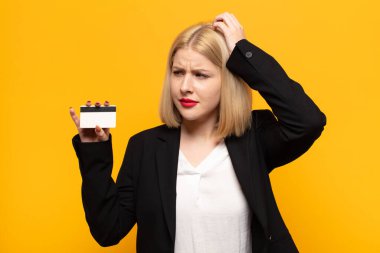 Sarışın kadın şaşkın ve şaşkın hissediyor, kafasını kaşıyor ve yan tarafa bakıyor.