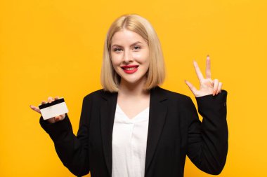 Sarışın kadın gülümsüyor ve arkadaş canlısı görünüyor, üç ya da üç numarayı gösteriyor, eli önde, geriye doğru sayıyor.