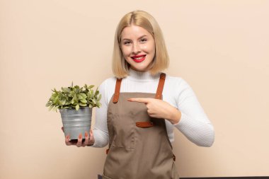 Sarışın kadın neşeyle gülümsüyor, mutlu hissediyor ve yan ve yukarı doğru işaret ediyor, fotokopi uzayındaki nesneleri gösteriyor.