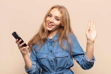 Sarışın kadın mutlu ve neşeyle gülümsüyor, el sallıyor, seni selamlıyor ya da hoşça kal diyor.