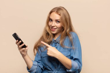 Sarışın kadın neşeyle gülümsüyor, mutlu hissediyor ve yan ve yukarı doğru işaret ediyor, fotokopi uzayındaki nesneleri gösteriyor.