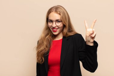 Sarışın kadın gülümsüyor ve arkadaş canlısı görünüyor. İki ya da iki numarayı gösteriyor. Elleri önde, geriye doğru sayıyor.