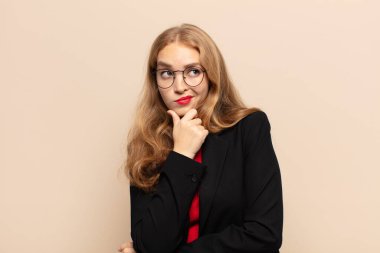 Sarışın kadın düşünüyor, kuşkulu ve şaşkın hissediyor, farklı seçenekleri var, hangi kararı vereceğini merak ediyor.