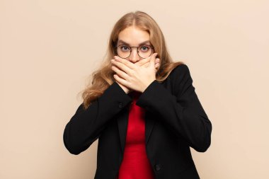 Sarışın kadın elleri ile ağzını kapatıyor, şok olmuş, şaşırmış bir ifadeyle, sır saklıyor ya da 