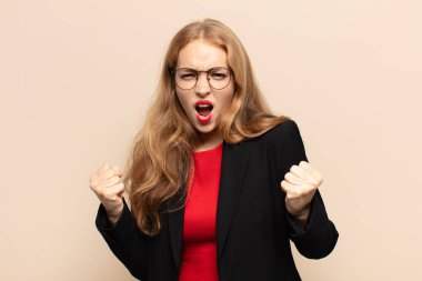 Sarışın kadın öfkeli bir ifadeyle ya da yumruklarıyla başarıyı kutlarken agresif bir şekilde bağırıyor.