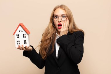 Sarışın kadın şok olmuş ve korkmuş hissediyor, ağzı açık ve elleri yanaklarında korkmuş görünüyor.