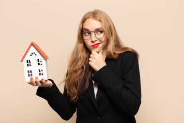 Sarışın kadın düşünüyor, kuşkulu ve şaşkın hissediyor, farklı seçenekleri var, hangi kararı vereceğini merak ediyor.