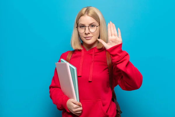 blonde woman looking serious, stern, displeased and angry showing open palm making stop gesture