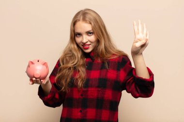 Sarışın kadın gülümsüyor ve arkadaş canlısı görünüyor, 4 ya da 4 numarayı gösteriyor, eli önde, geriye doğru sayıyor.