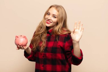 Sarışın kadın mutlu ve neşeyle gülümsüyor, el sallıyor, seni selamlıyor ya da hoşça kal diyor.