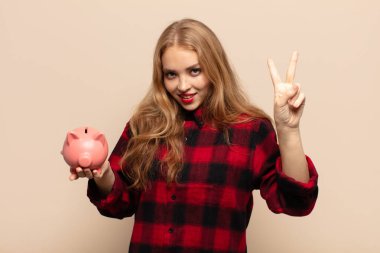 Sarışın kadın gülümsüyor ve arkadaş canlısı görünüyor. İki ya da iki numarayı gösteriyor. Elleri önde, geriye doğru sayıyor.