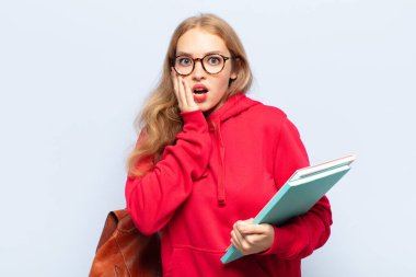 Sarışın kadın şok olmuş ve korkmuş hissediyor, ağzı açık ve elleri yanaklarında korkmuş görünüyor.