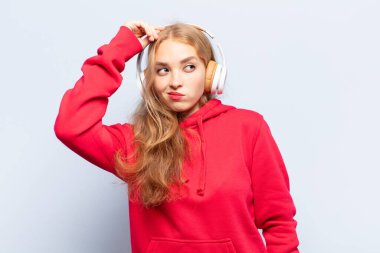 Sarışın kadın şaşkın ve şaşkın hissediyor, kafasını kaşıyor ve yan tarafa bakıyor.