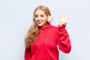 Sarışın kadın gülümsüyor ve arkadaş canlısı görünüyor, üç ya da üç numarayı gösteriyor, eli önde, geriye doğru sayıyor.