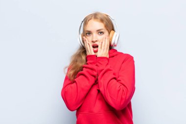 Sarışın kadın şok olmuş ve korkmuş hissediyor, ağzı açık ve elleri yanaklarında korkmuş görünüyor.