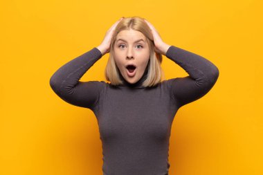 Sarışın kadın heyecanlı ve şaşırmış görünüyor, ağzı açık, elleri başının üstünde, şanslı bir kazanan gibi hissediyor.