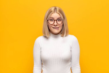 Sarışın kadın şaşkın ve şaşkın görünüyor. Sinirli bir hareketle dudağını ısırıyor. Sorunun cevabını bilmiyor.