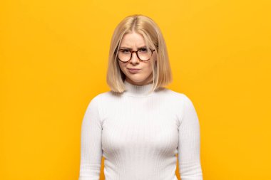 Sarışın kadın şaşkın ve şüpheli hissediyor, merak ediyor ya da karar vermeye çalışıyor.