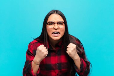 Sinirli, hayal kırıklığına uğramış, kızgın bakışlar ve sıkı yumruklarla bağıran Latin bir kadın.