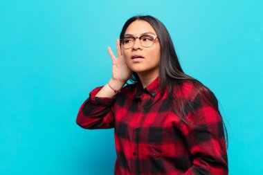 Latin kadın gülümsüyor, tuhaf bir şekilde yan tarafa bakıyor, dedikoduları dinlemeye ya da bir sırrı duymaya çalışıyor.