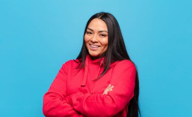 Kollarını kavuşturup mutlu bir şekilde gülen Latin bir kadın, rahat, olumlu ve tatmin edici bir pozla.