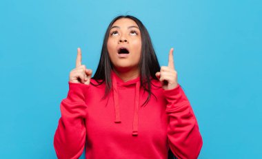 Latin bir kadın şaşırmış, şaşırmış ve ağzı açık bir şekilde iki eliyle boşluğu kopyalamak için yukarı bakıyor.