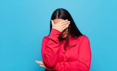 Latin bir kadın stresli, utanmış ya da üzgün görünüyor, baş ağrısı var, yüzünü eliyle kapatıyor.