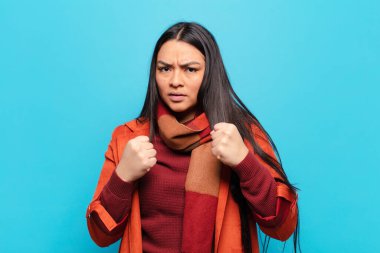 Kendinden emin, sinirli, güçlü ve agresif görünen Latin bir kadın. Yumrukları boks pozisyonunda dövüşmeye hazır.