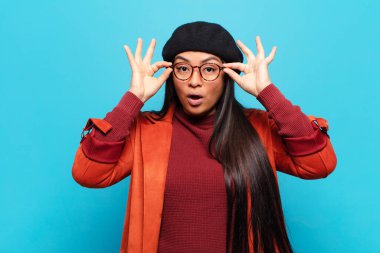 Latin kadın şaşkın, şaşkın ve şaşırmış hissediyor, elinde şaşkın, inançsız bir bakışla gözlük tutuyor.